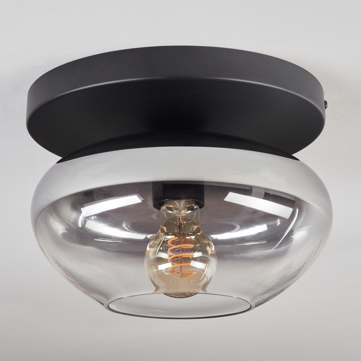 Moderne Deckenleuchte mit schwarzem Sockel, Glas-Lampenschirm und sichtbarer Glühbirne.