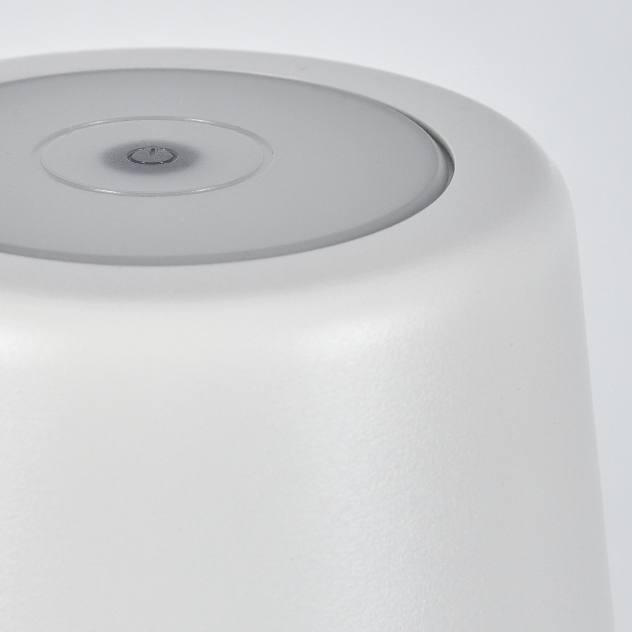 Naheaufnahme einer weißen zylindrischen Lampe mit einem durchscheinenden oberen Ring und einem Ein/Aus-Symbol.
