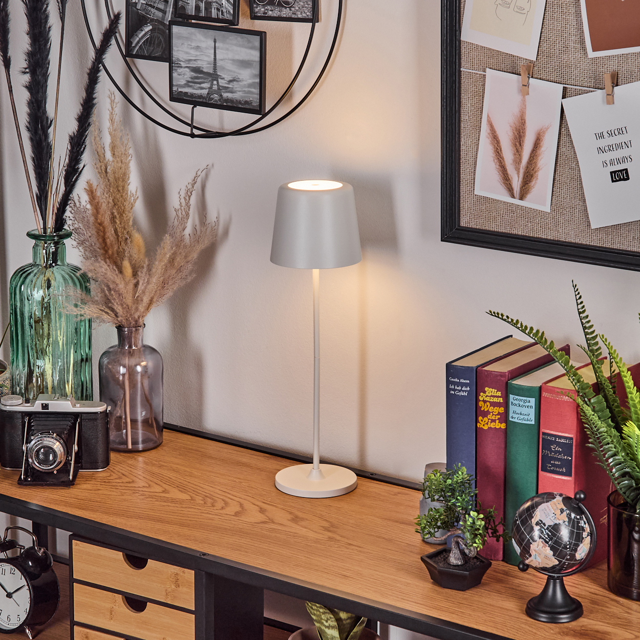 Ein Schreibtisch mit Lampe, Büchern, Pflanzen, einer Kamera und Dekorationen.