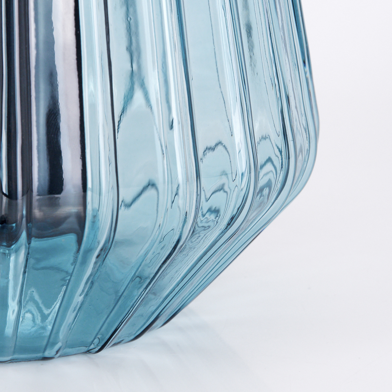 Ein blauer Glasbehälter mit vertikalen Rillen auf weißem Hintergrund.