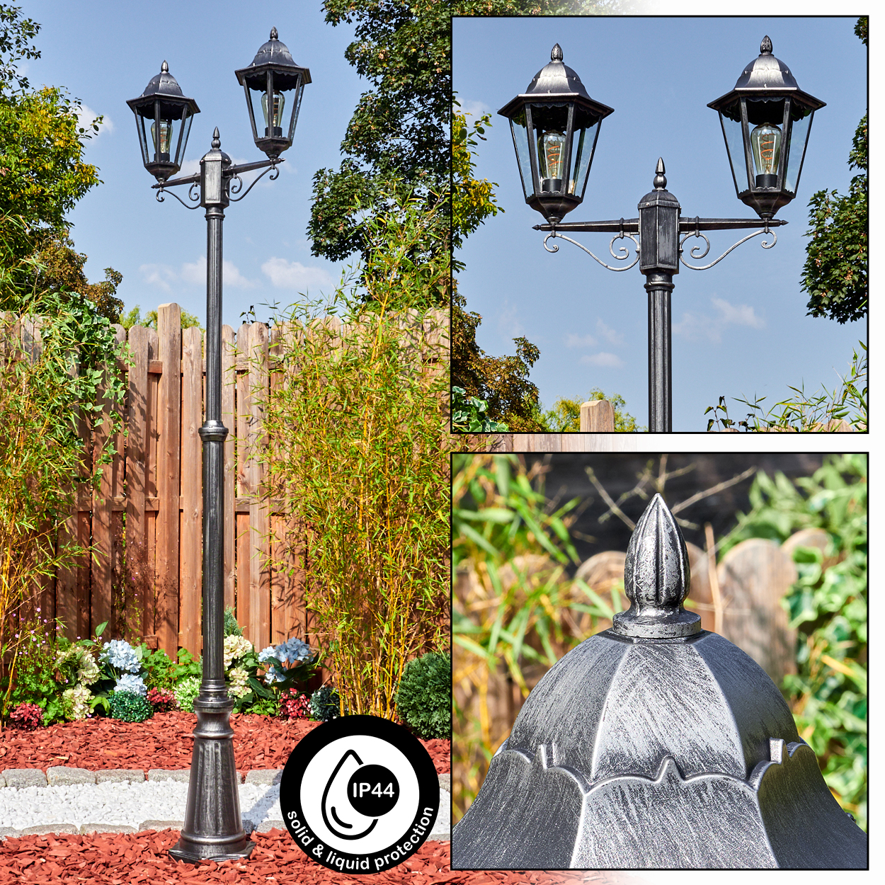 Eine dunkle Gartenlaterne mit zwei Lampen steht auf einem Sockel inmitten von Pflanzen.