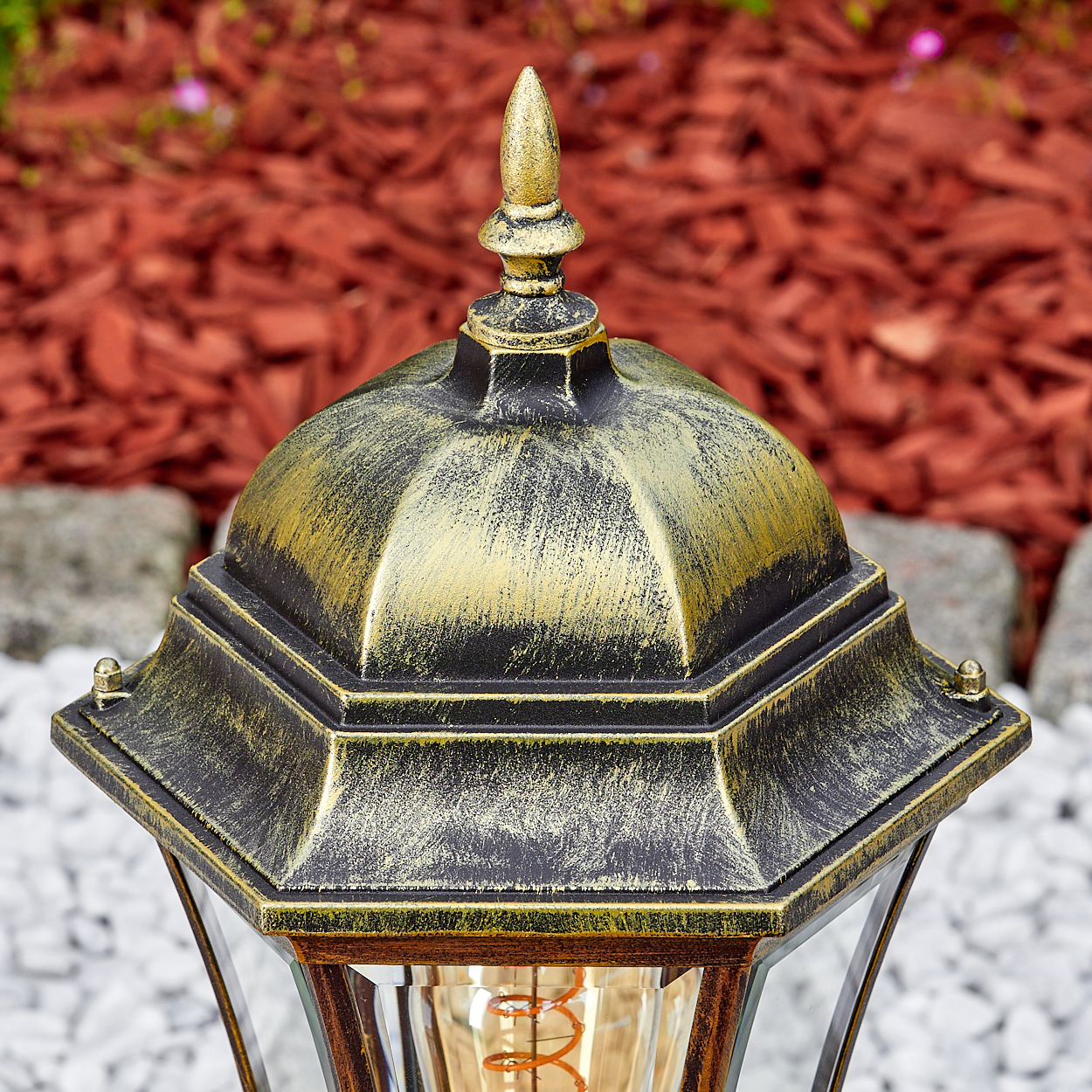 Goldene Lampe mit Glühfaden im Freien auf Kies und Rindenmulch.