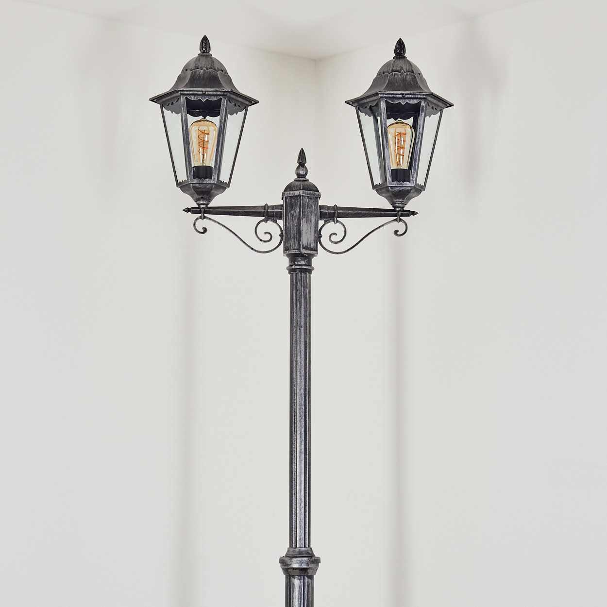 Eine silberne Stehlampe mit zwei Laternenköpfen und Glühbirnen.