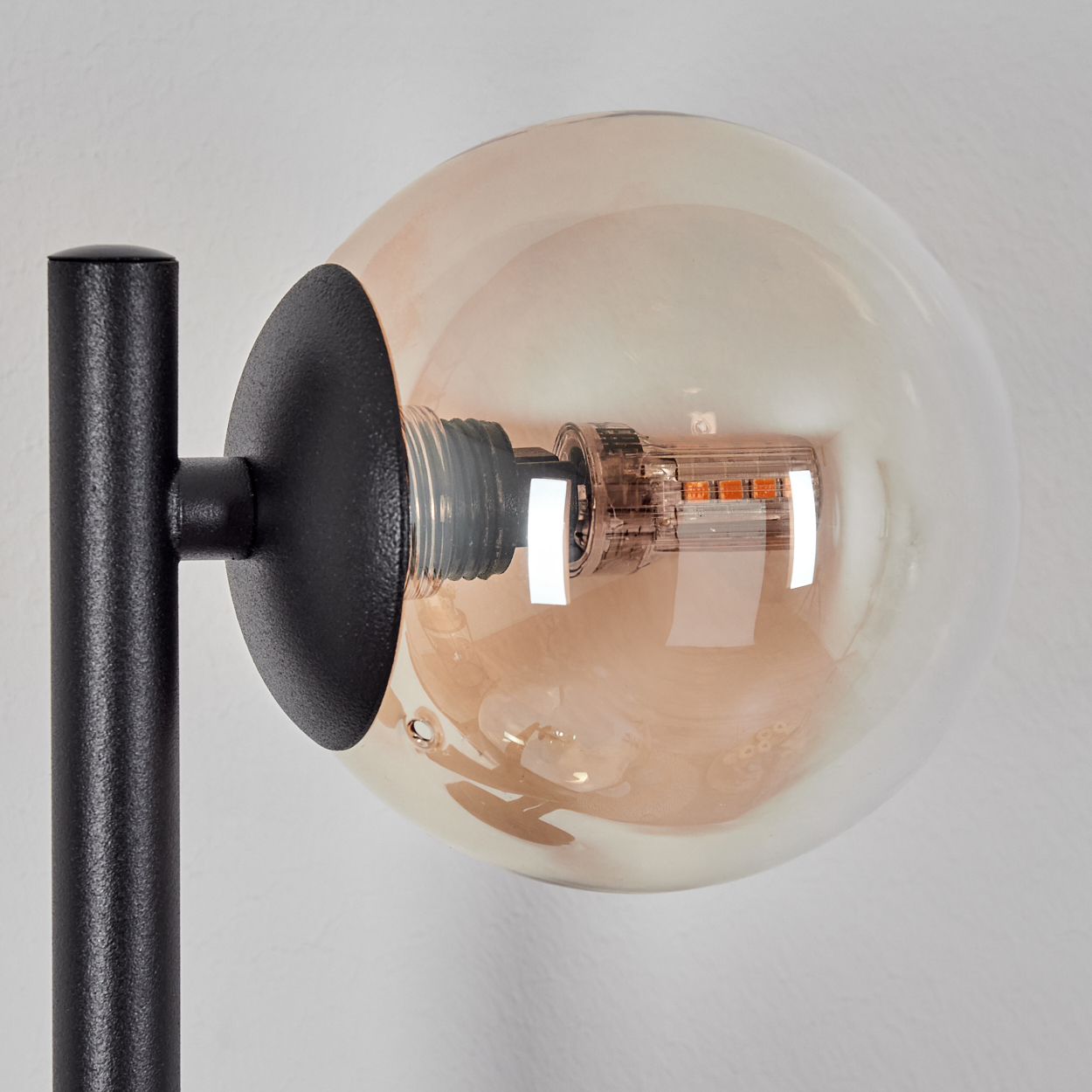 Eine kugelförmige bernsteinfarbene Glühbirne mit sichtbaren LEDs, montiert an einem schwarzen Lampenarm.