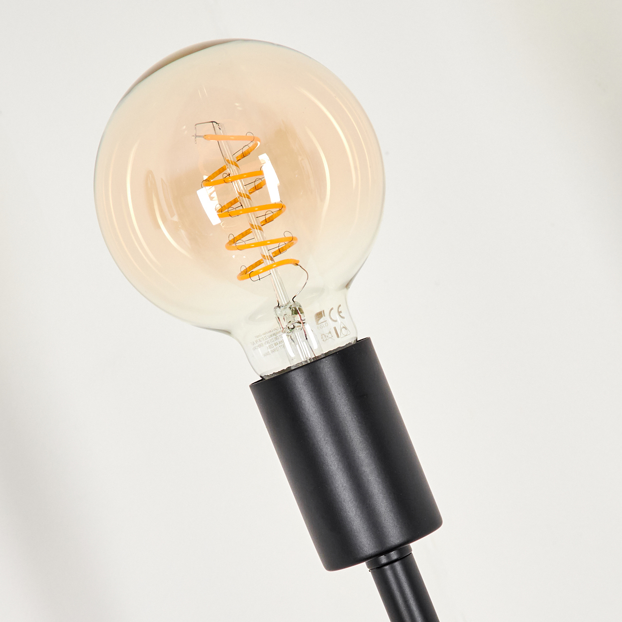Nahaufnahme einer Edison-Glühbirne im Vintage-Stil mit Spulenfilament, an schwarzem Sockel befestigt.