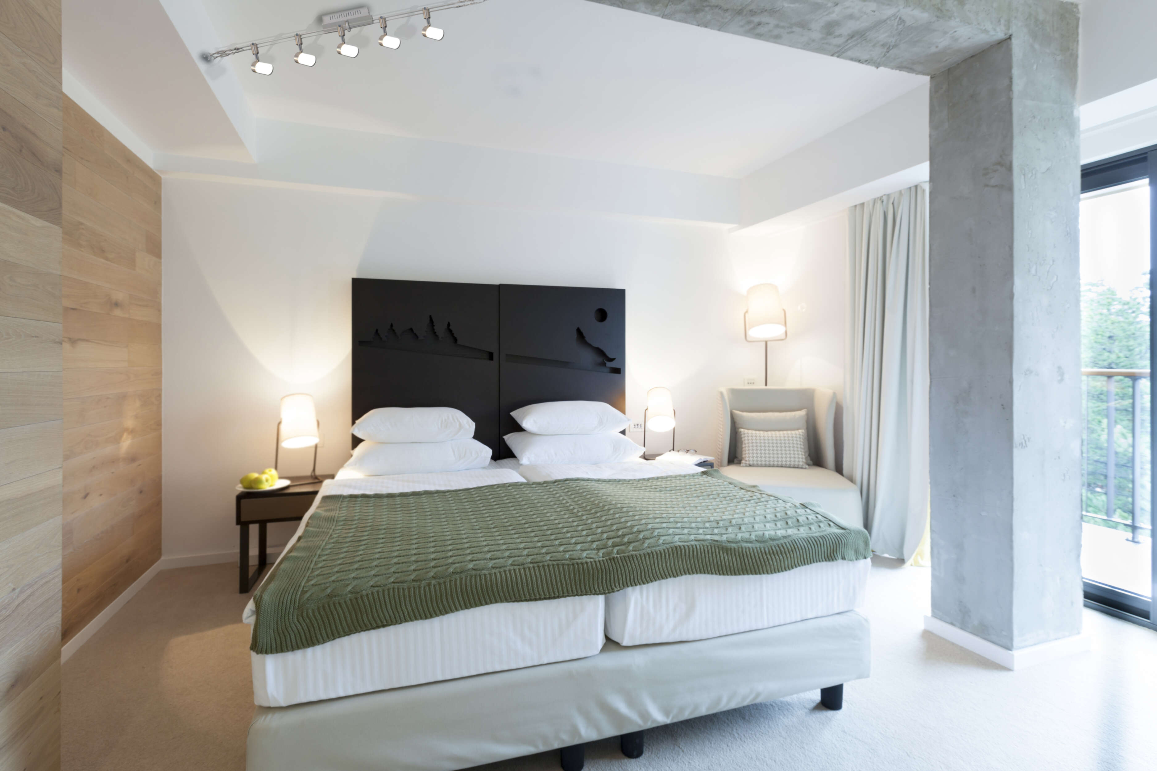 Ein Doppelbett mit grüner Decke, weißen Kissen und Holzwand.