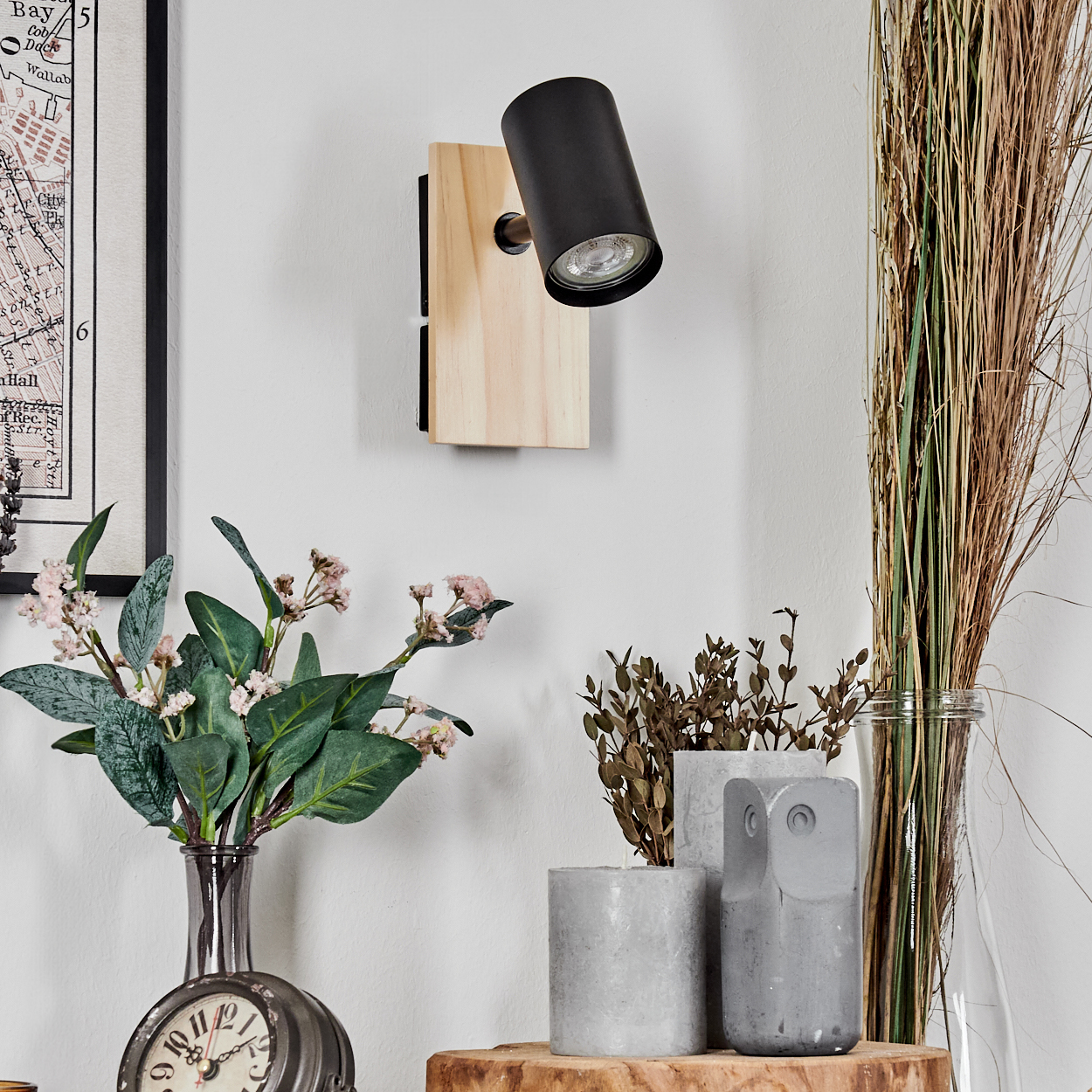 Ein schwarzer Wandspot auf Holz montiert, mit Blumen und Dekorationsgegenständen.