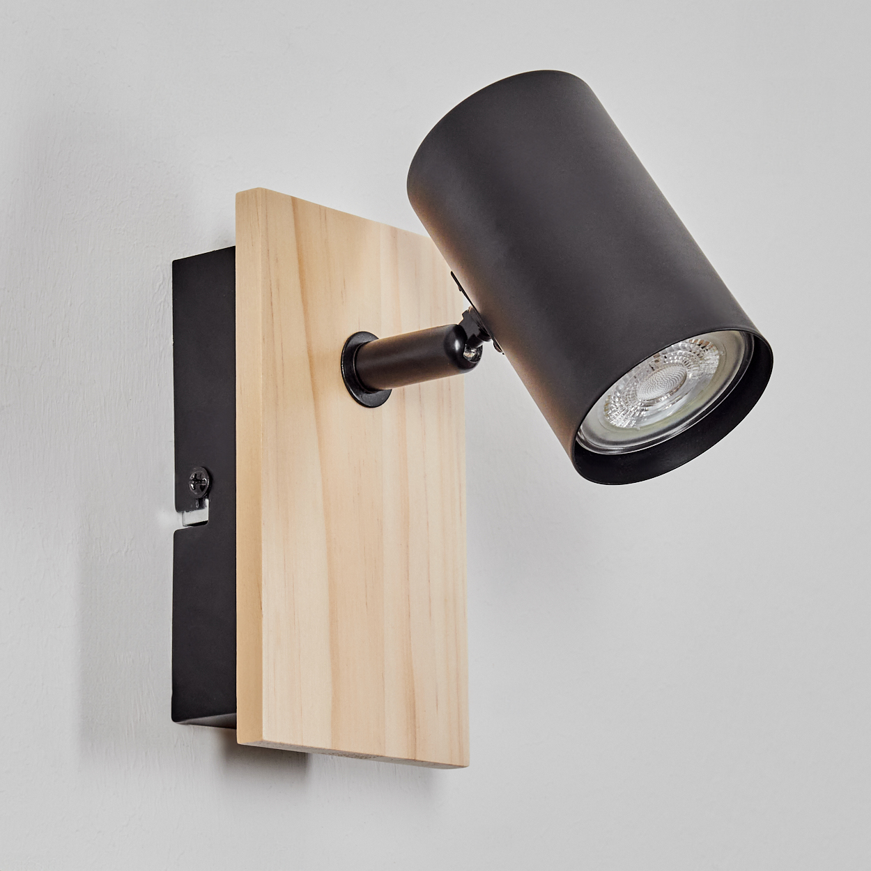 Schwarzer Strahler mit Holzplatte an weißer Wand.