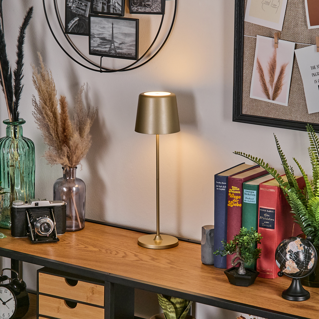 Ein goldener Tischlampen-Schreibtisch mit Büchern, Pflanzen und einer Kamera.