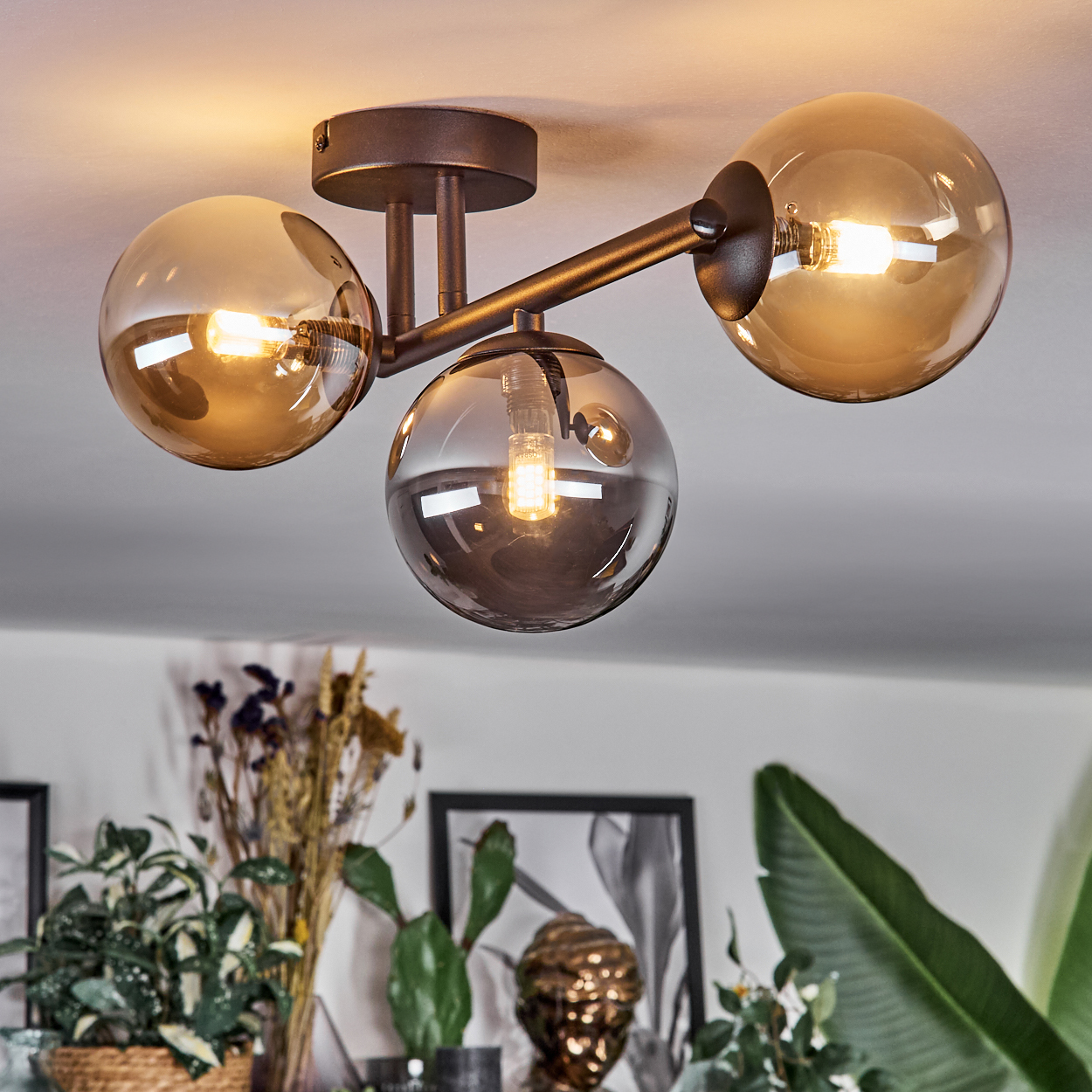 Eine Deckenleuchte mit drei rauchglas-Kugeln und Glühbirnen auf dunklem Metallgestell.