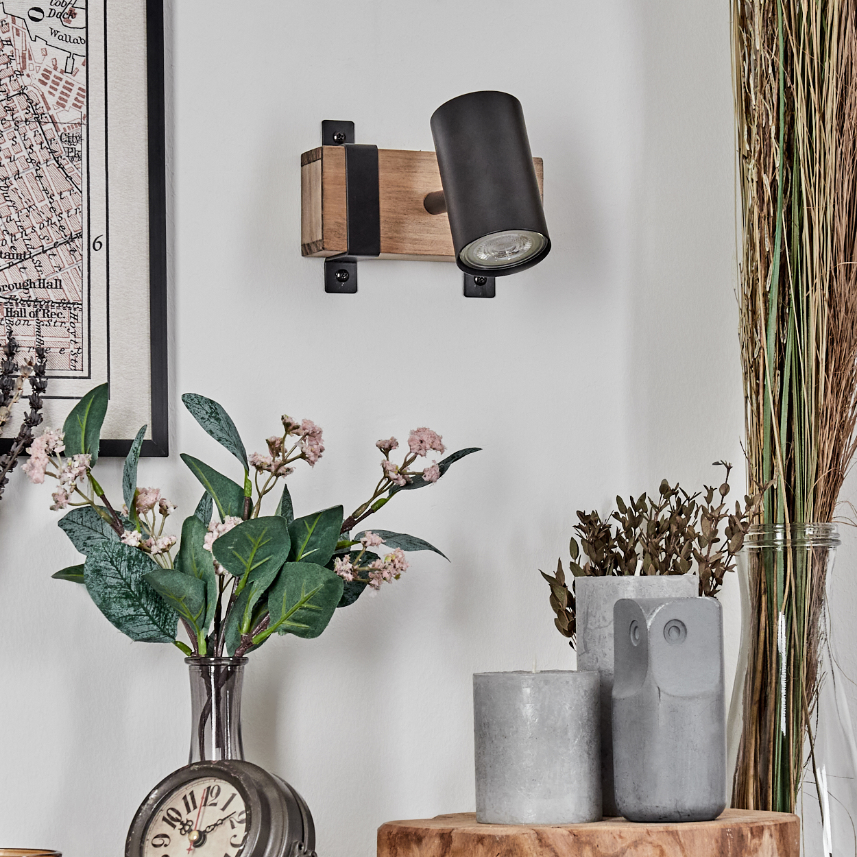 Eine Wandleuchte aus Holz und Metall über Blumen und Kerzen.