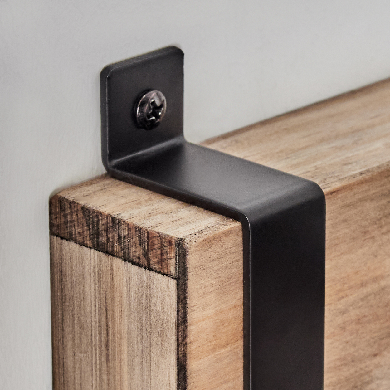 Ein schwarzer Metallwinkel ist mit einer Schraube an einer Holzkante befestigt.