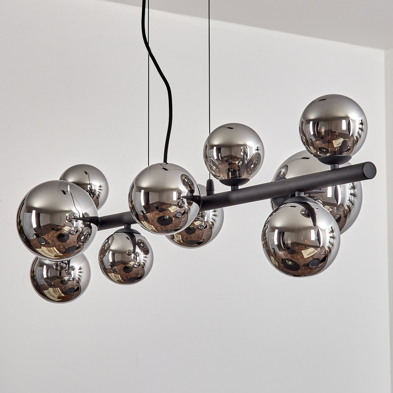 Eine moderne Pendelleuchte mit neun glänzenden, kugelförmigen Lampenschirmen in Dunkelgrau.