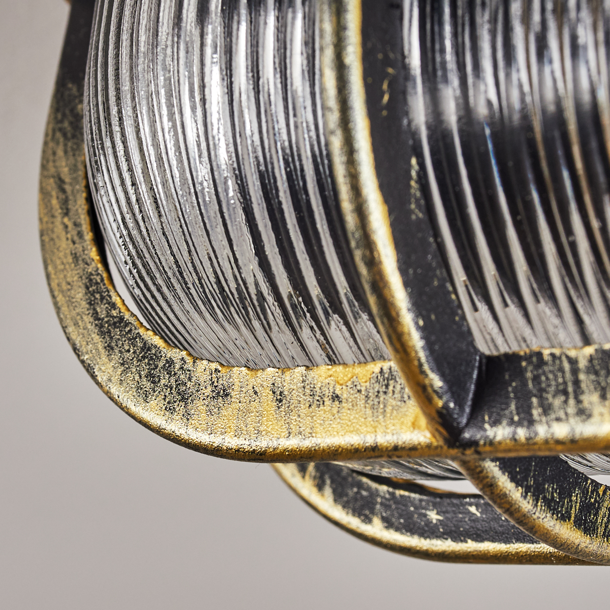 Detailaufnahme einer Lampe mit geriffeltem Glas und gold-schwarzem Metallrahmen.