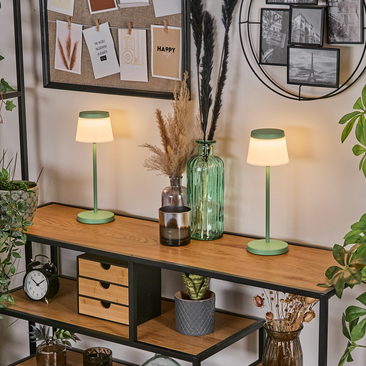 Zwei grüne Tischlampen auf einem Holzregal, dekoriert mit Vasen und Pflanzen.