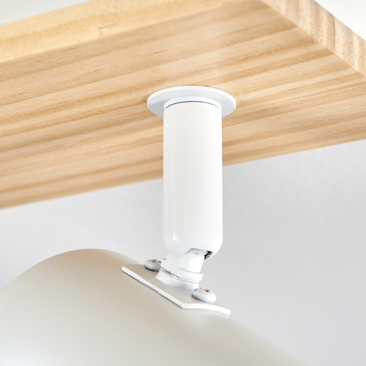 Eine weiße Halterung verbindet eine weiße Lampe mit einem Holzregal.