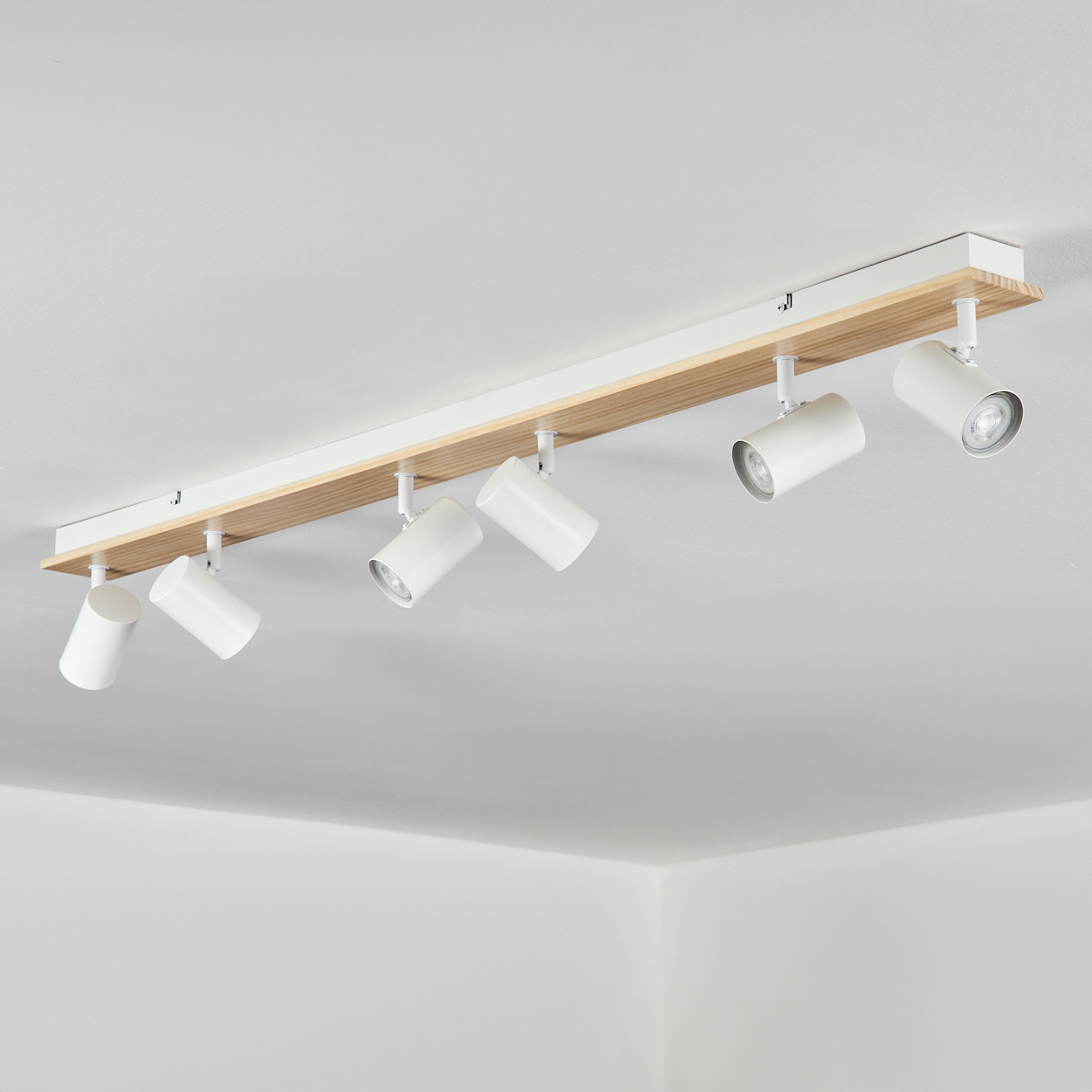 Weiße Deckenleuchte mit sechs Spots auf Holzbasis, an weißer Decke montiert.