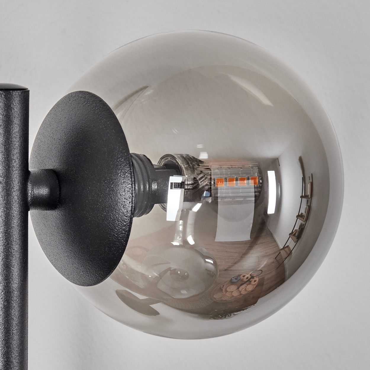 Eine graue Glühbirne mit sichtbaren orangen LEDs und Spiegelungen eines Raumes.