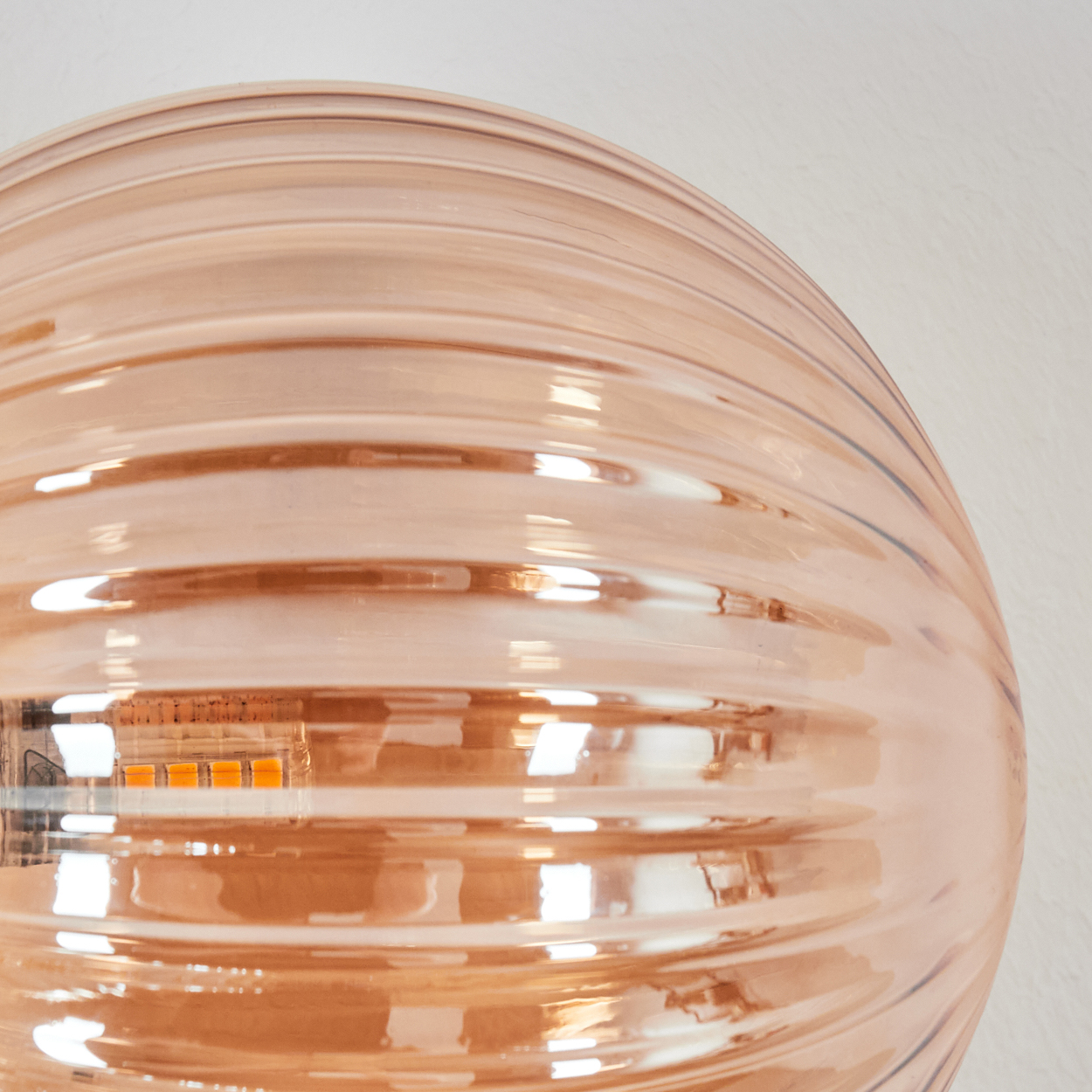 Orangefarbene Glaslampe mit horizontalen Rillen und sichtbaren LEDs.