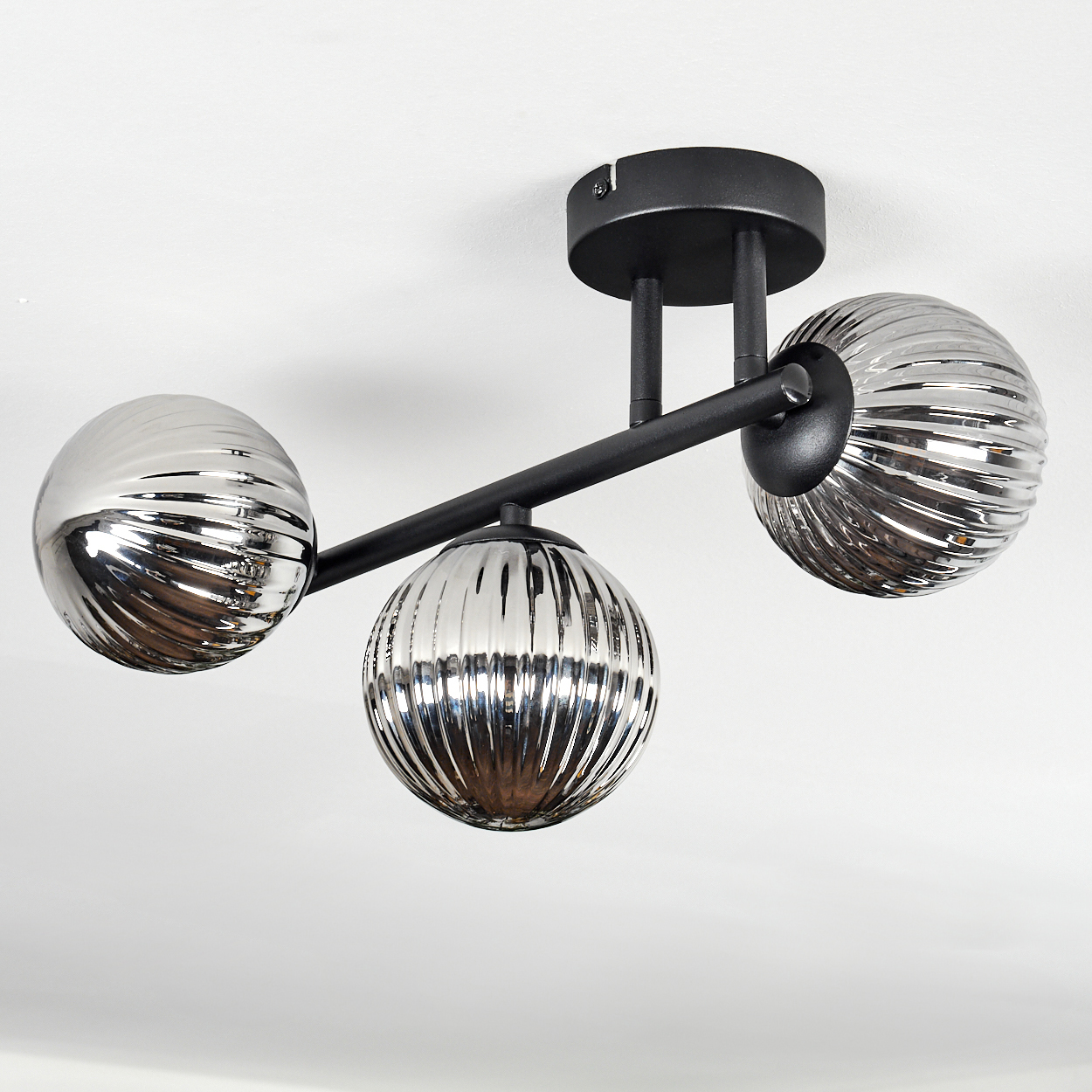 Schwarze Deckenleuchte mit drei kugelförmigen, gerippten Glasschirmen in Metallic-Optik.