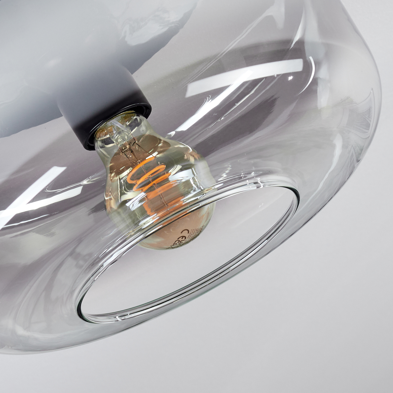 Eine Glühbirne mit Spiralfilament in einem transparenten, grauen Glaslampenschirm.