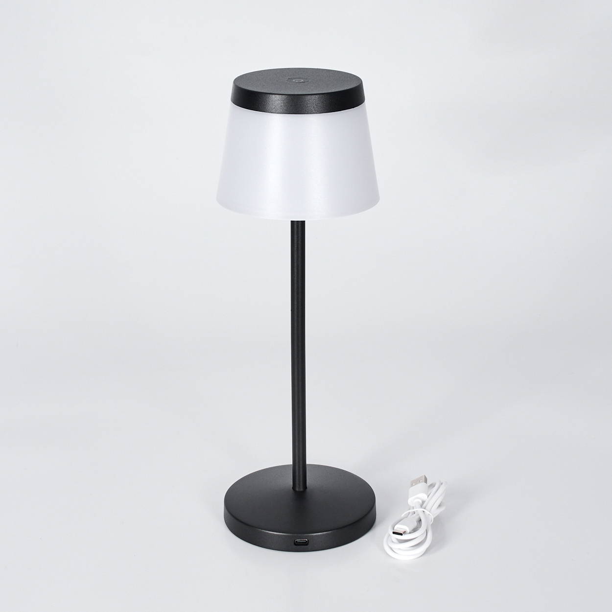 Schwarze Tischlampe mit weißem Schirm, neben einem weißen USB-Kabel.