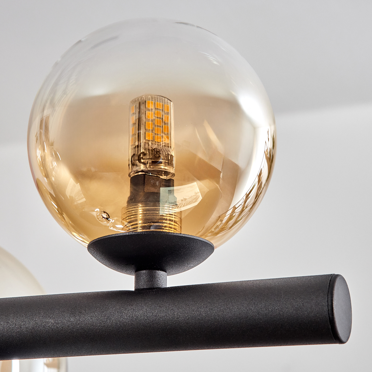 Eine bernsteinfarbene Glaskugel mit LED-Birne auf einem schwarzen Metallarm.