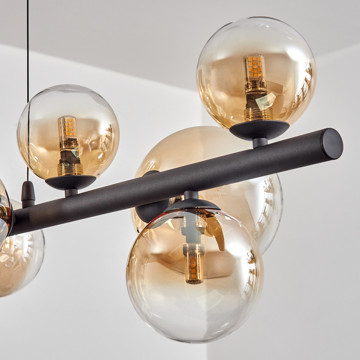 Moderne Hängelampe mit bernsteinfarbenen Glaskugeln und schwarzem Metallrahmen.