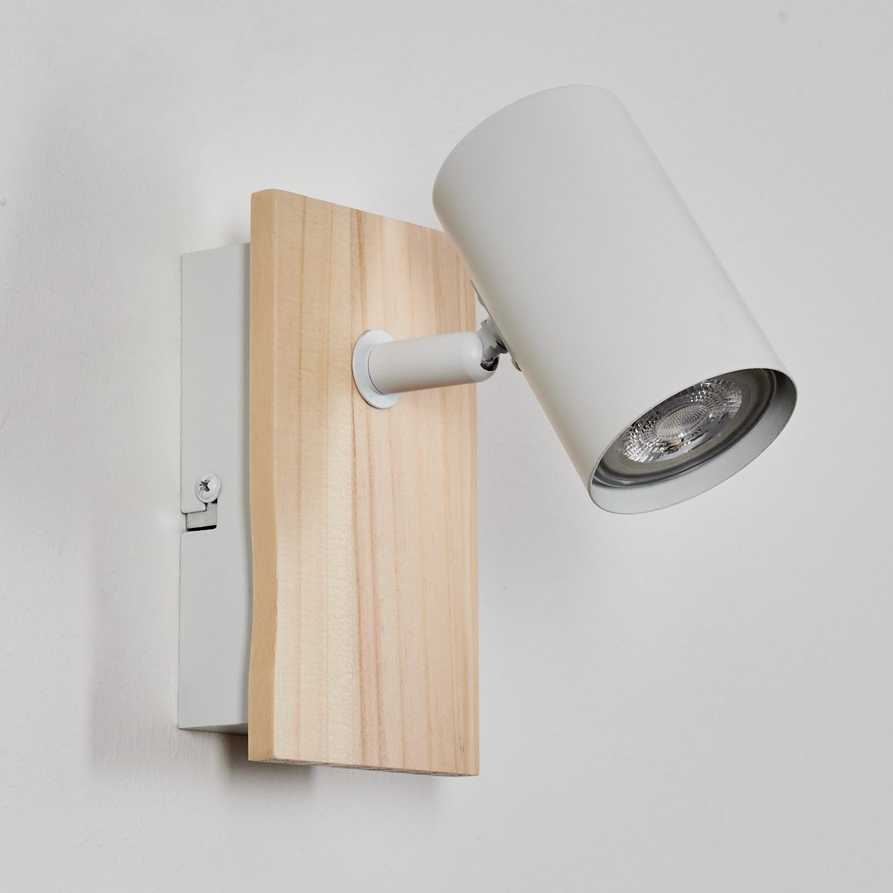 Eine weiße Lampe mit Holzsockel an einer weißen Wand.