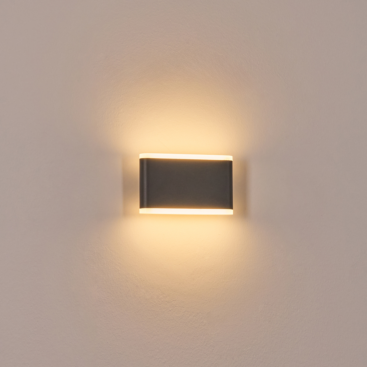 Eine dunkle rechteckige Wandleuchte mit warmweißer Beleuchtung an einer hellen Wand.
