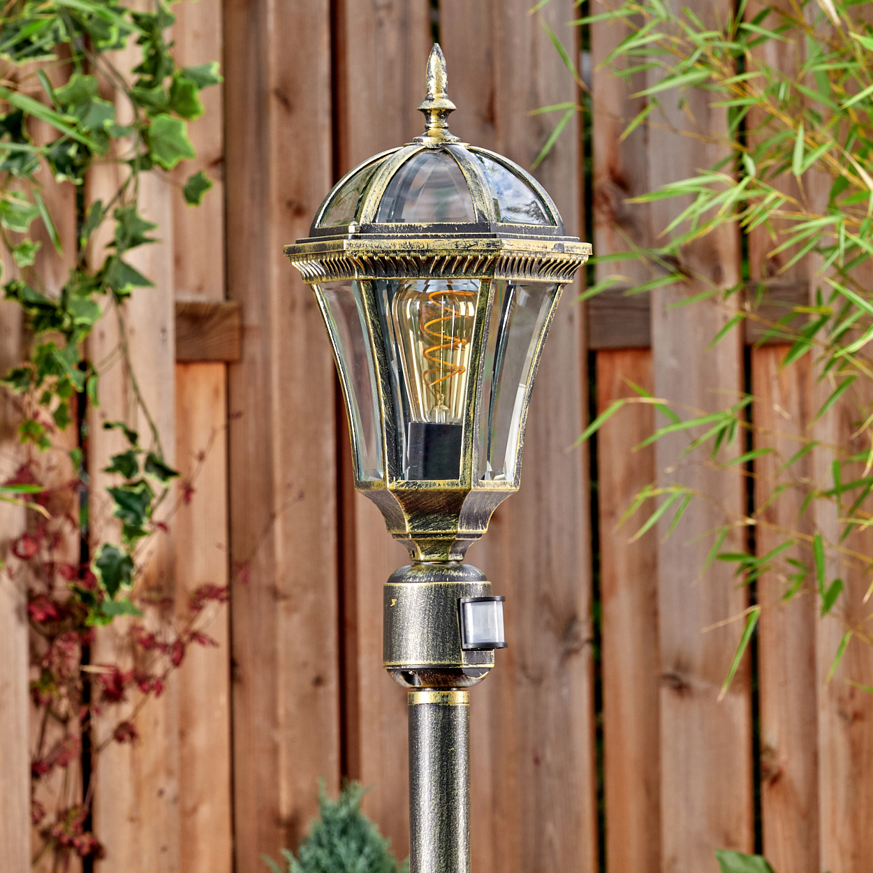 Ein antiker Gartenlichtmast mit einem sichtbaren Glühfaden und Holzzaun.