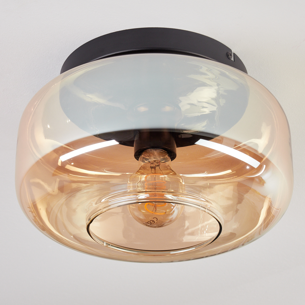 Eine Deckenleuchte mit einem schwarzen Sockel und einem bernsteinfarbenen Glas. Ein Glühfaden ist sichtbar.