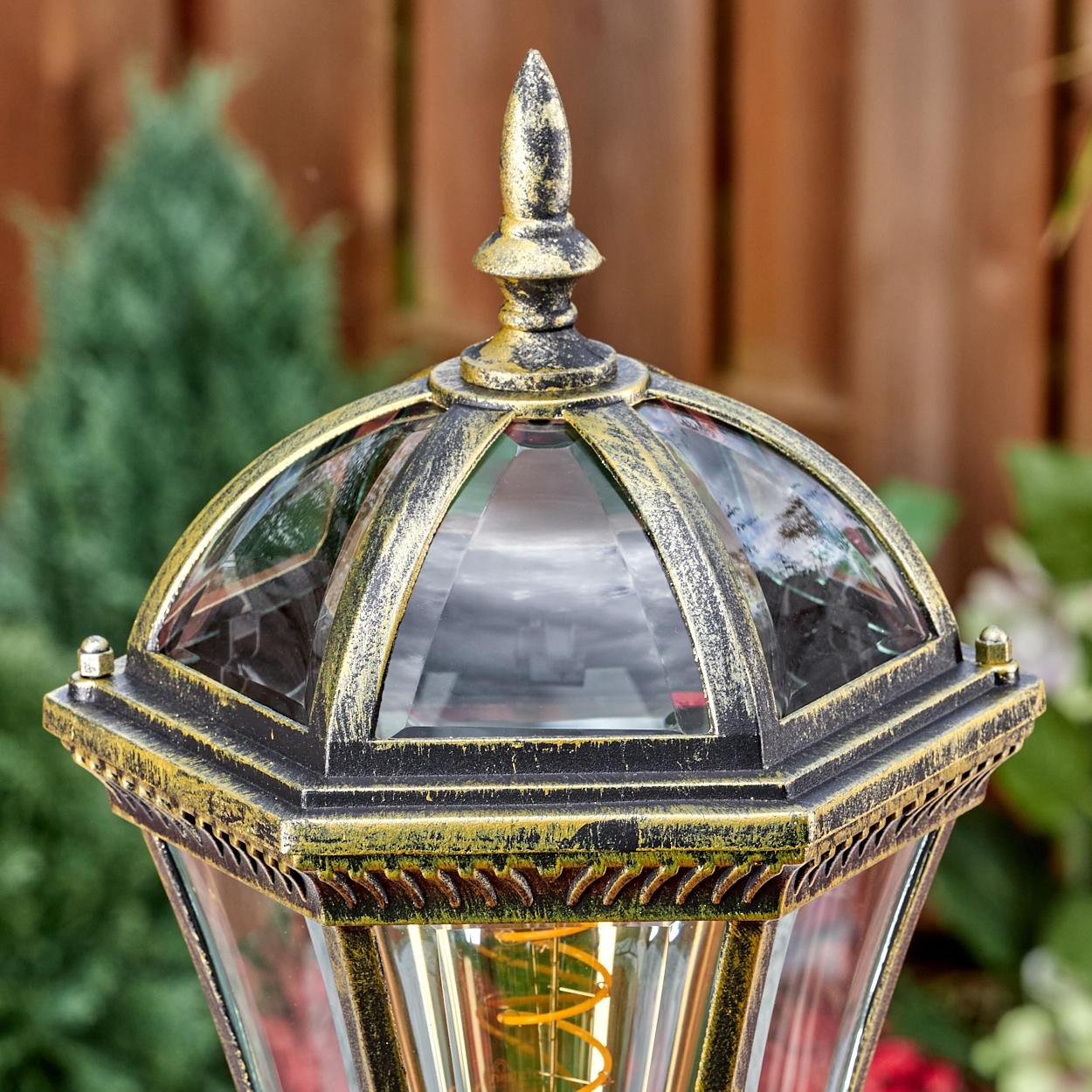 Detail einer verzierten Gartenlaterne mit Glas und Glühfaden.