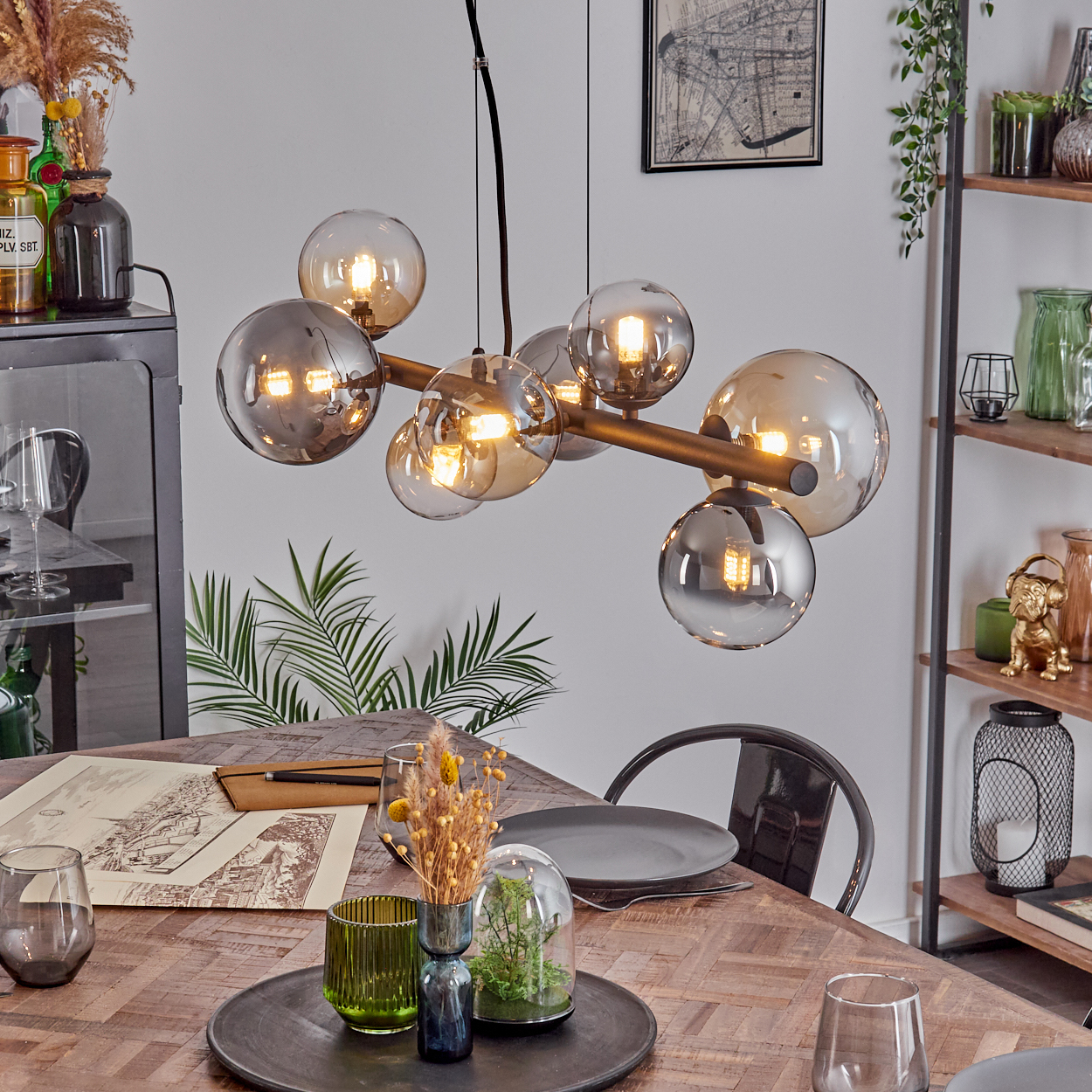 Moderne Hängelampe mit Glaskugeln über einem Holztisch mit Dekorationen.