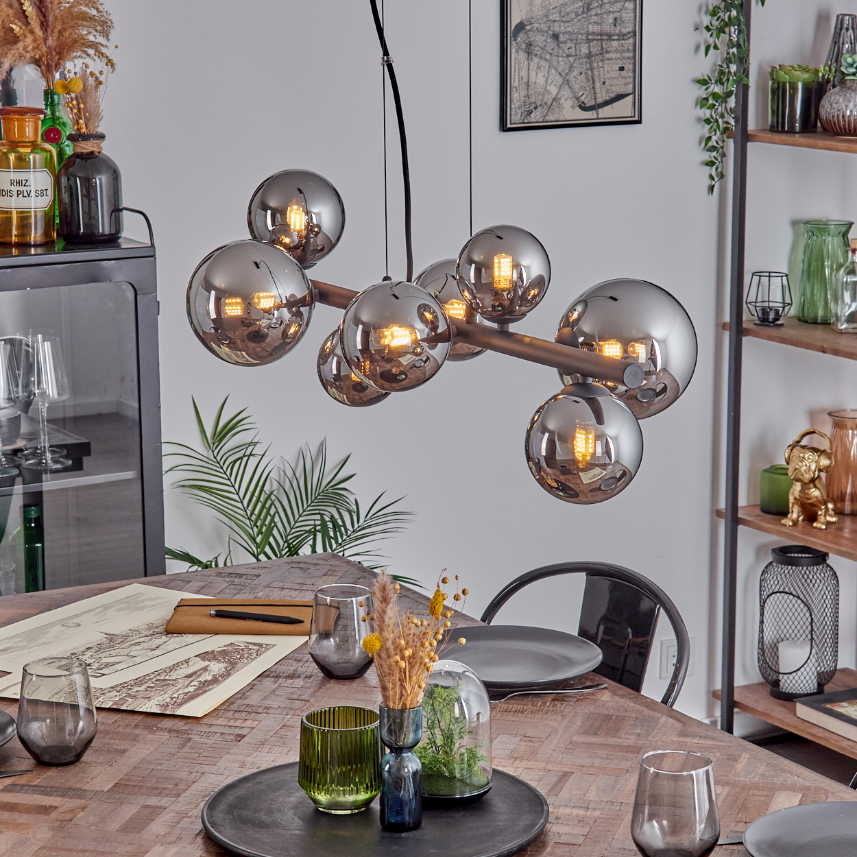 Eine moderne Pendelleuchte mit Glaskugeln über einem Holztisch mit Geschirr und Pflanzen.