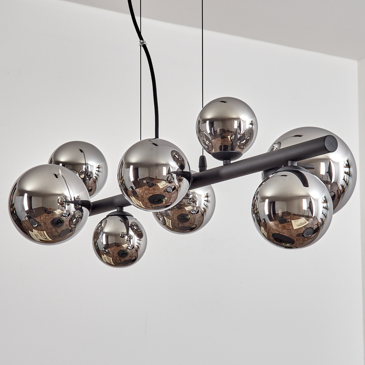 Eine moderne Lampe mit acht glänzenden silbernen Kugeln an einem schwarzen Stab.