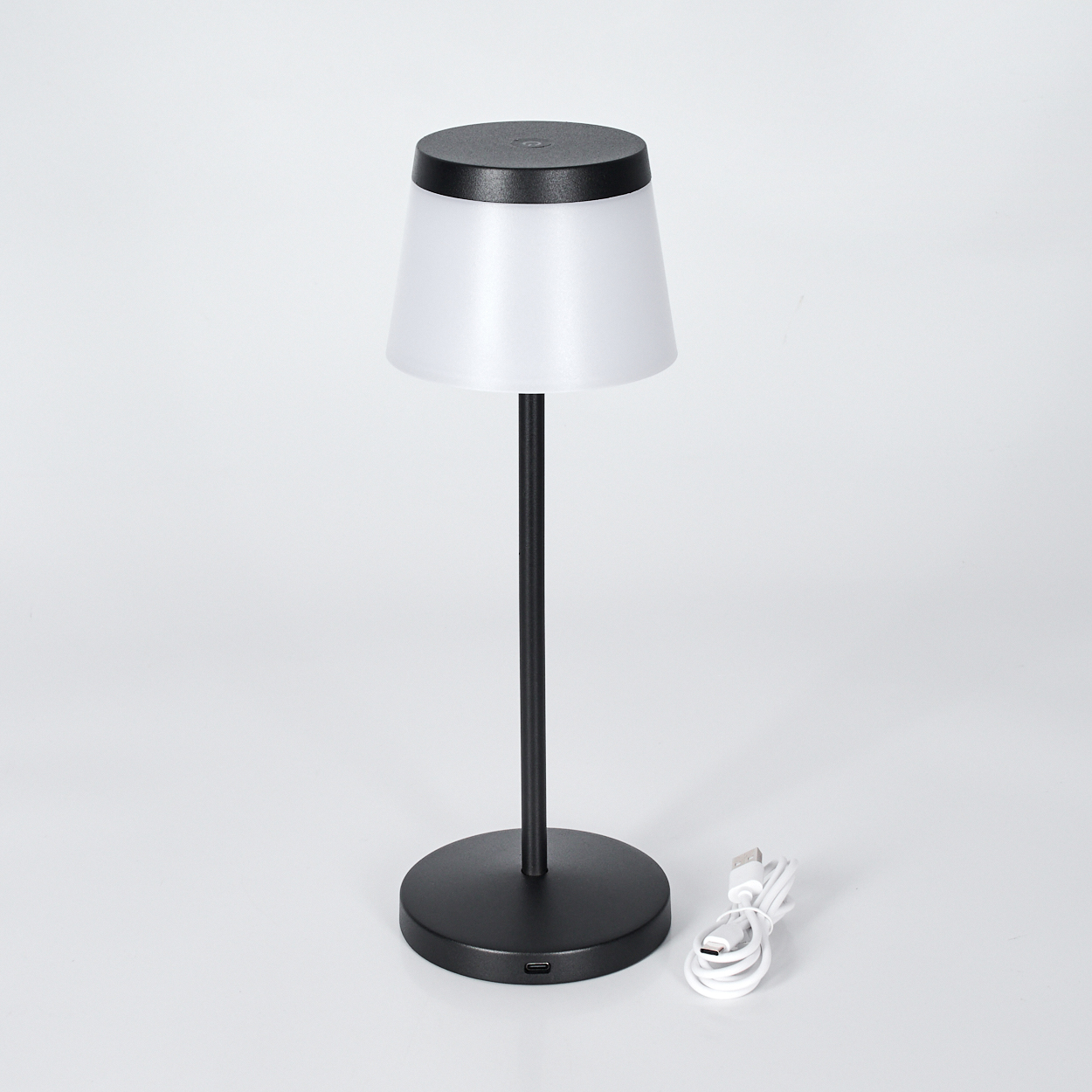 Eine schwarze Tischlampe mit weißem Schirm und USB-Kabel.