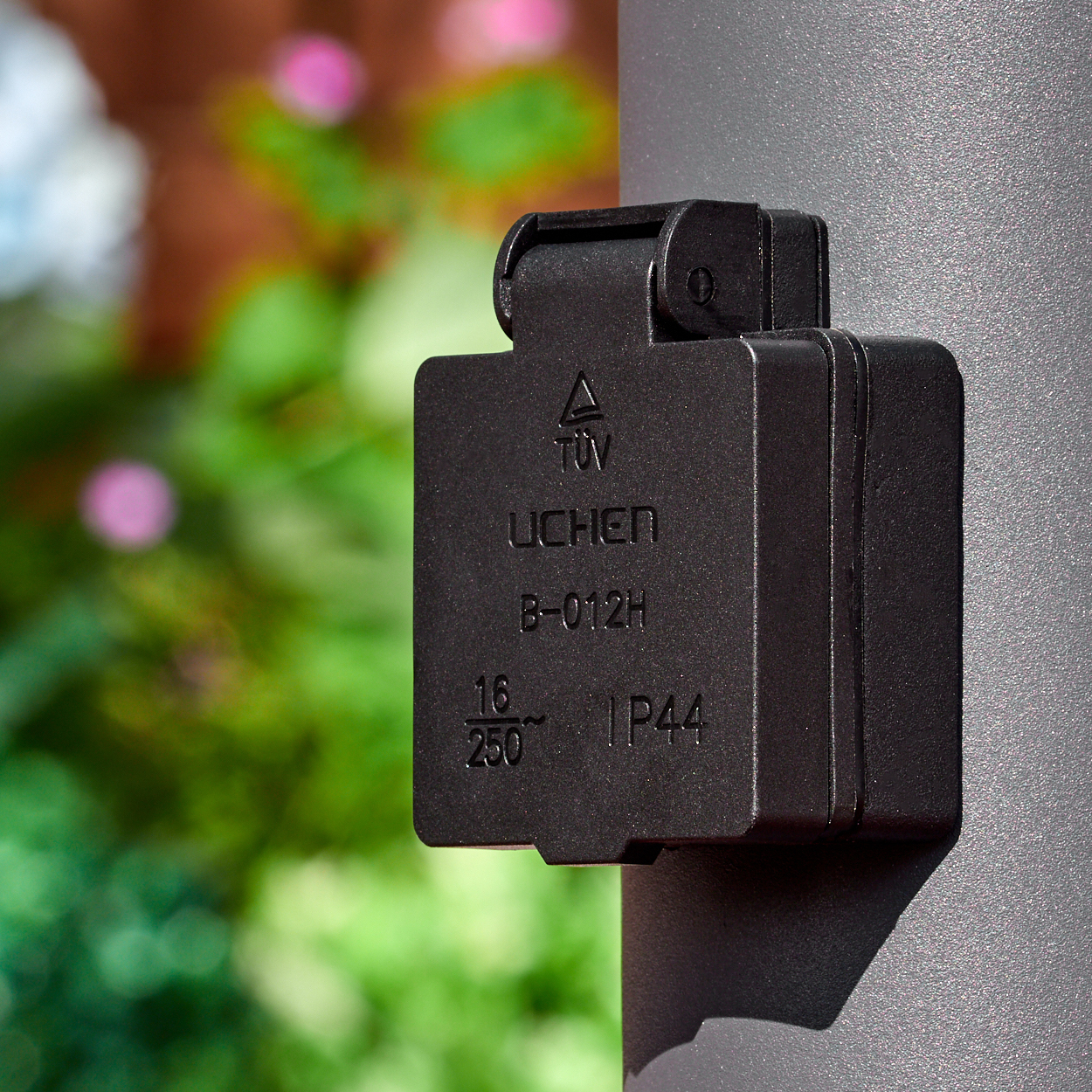 Schwarzer Stecker mit IP44-Schutz, befestigt an einem Mast, mit grünem Hintergrund.