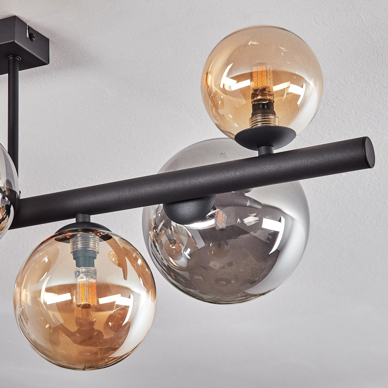 Eine moderne Deckenleuchte mit schwarzen Metallarmen und Glaskugeln in Bernstein und Rauchglas.