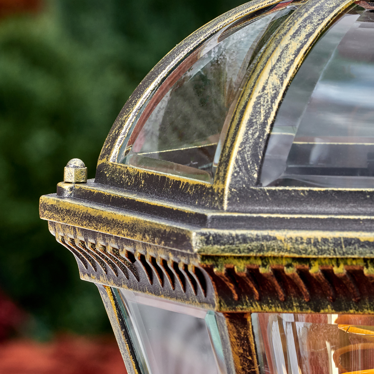 Detail einer verzierten Laterne mit goldener Patina auf dunklem Metall.