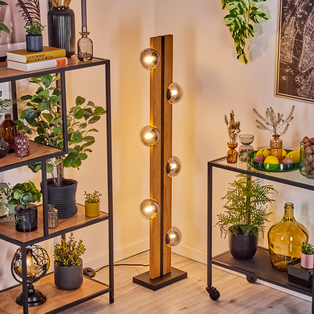 Ein hoher Holz-Bodenlicht mit Glaskugeln steht neben einem Regal voller Pflanzen und Deko.