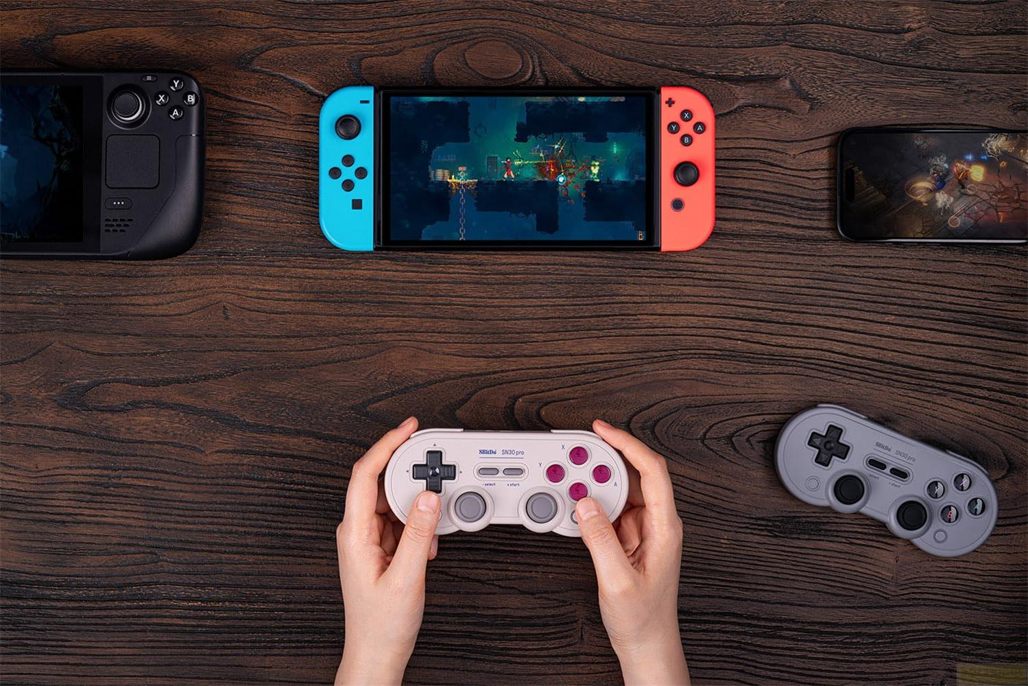 Quattro dispositivi da gioco su superficie in legno: Steam Deck, Switch, telefono e controller.
