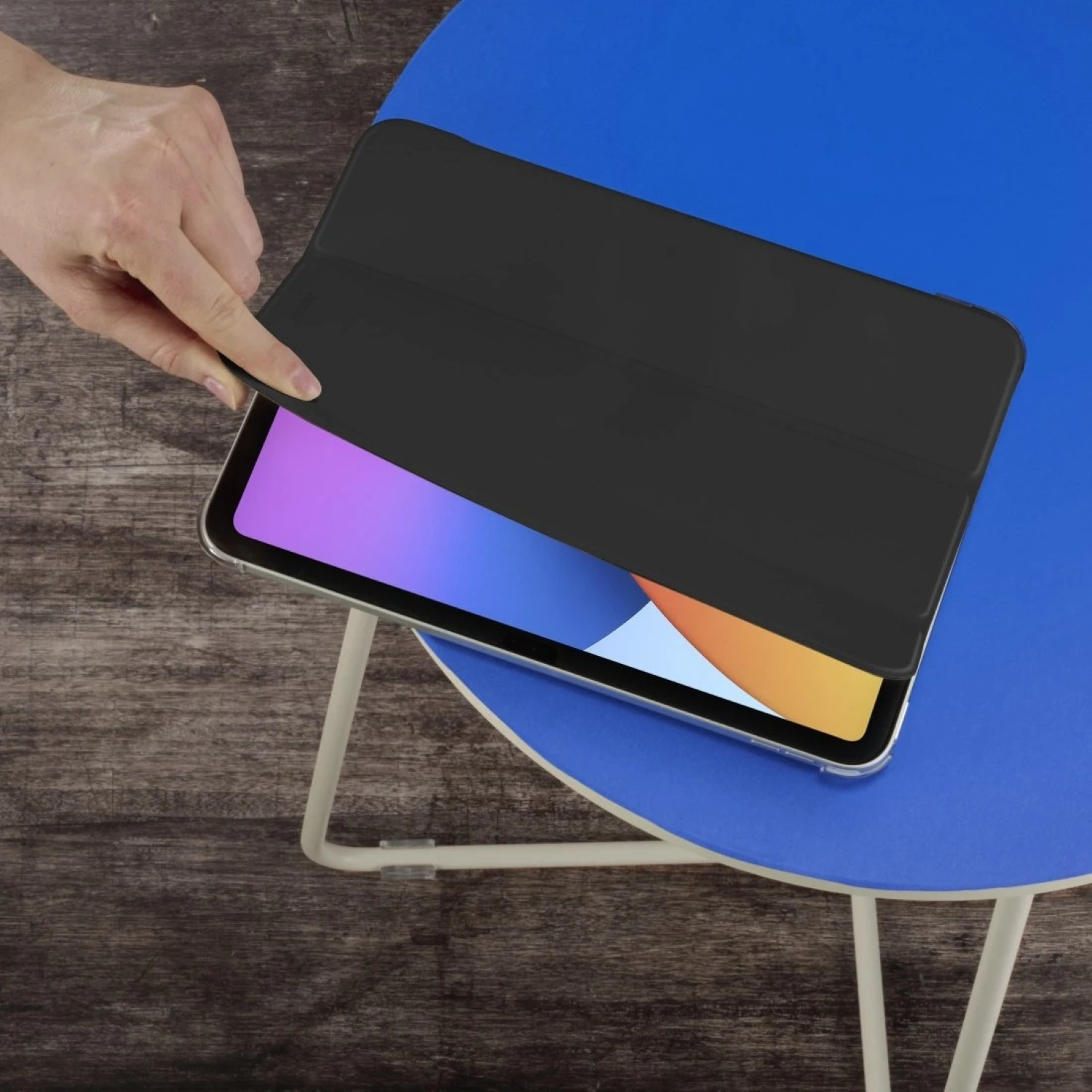 Eine Hand schließt eine schwarze Hülle über einem Tablet auf einem blauen Tisch.