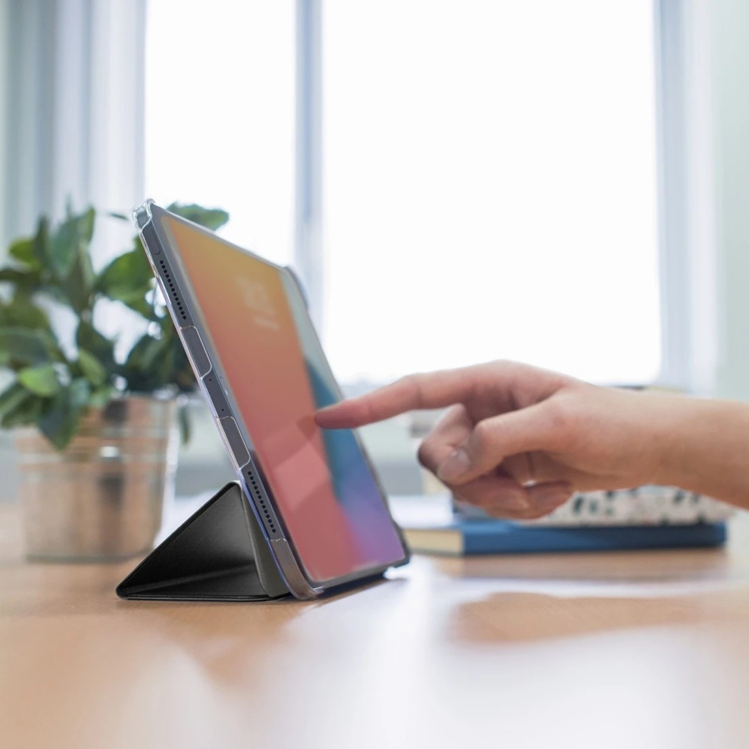 Eine Hand berührt einen Tablet-Bildschirm, der auf einem Tisch steht.