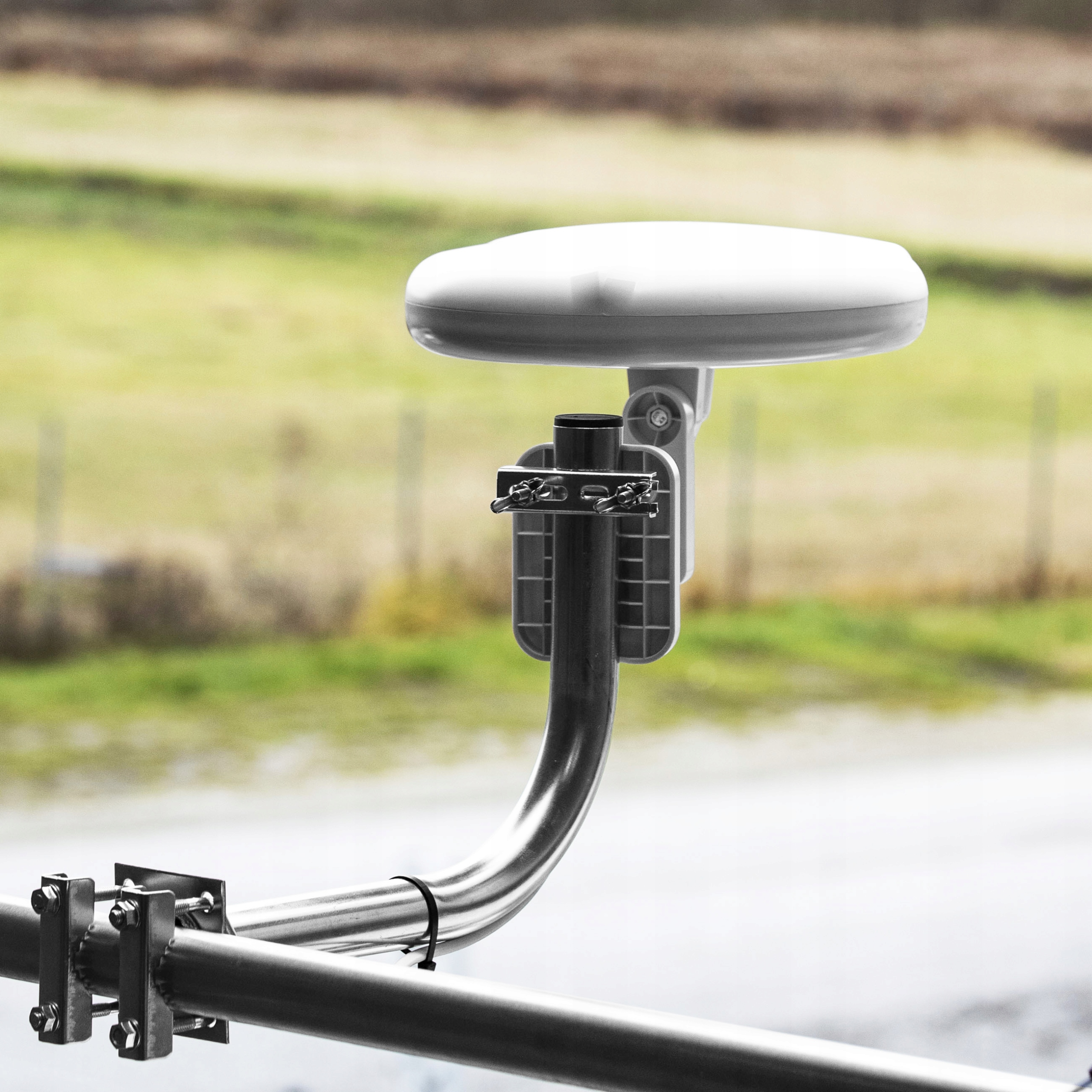 Biała antena satelitarna zamontowana na metalowym maszcie. Na zewnątrz jest zielono.