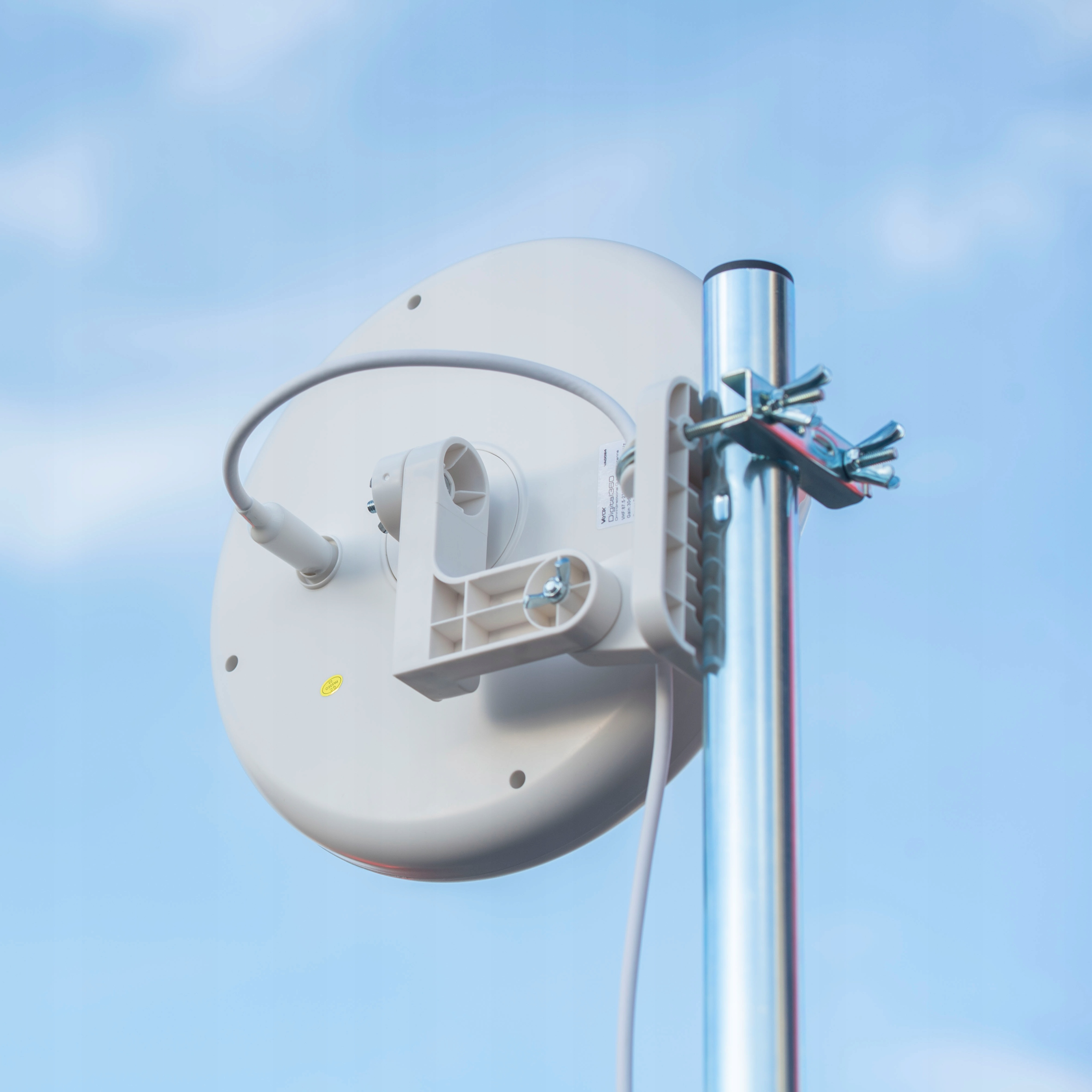Biały emiter anteny zamontowany na słupie, na tle błękitnego nieba.