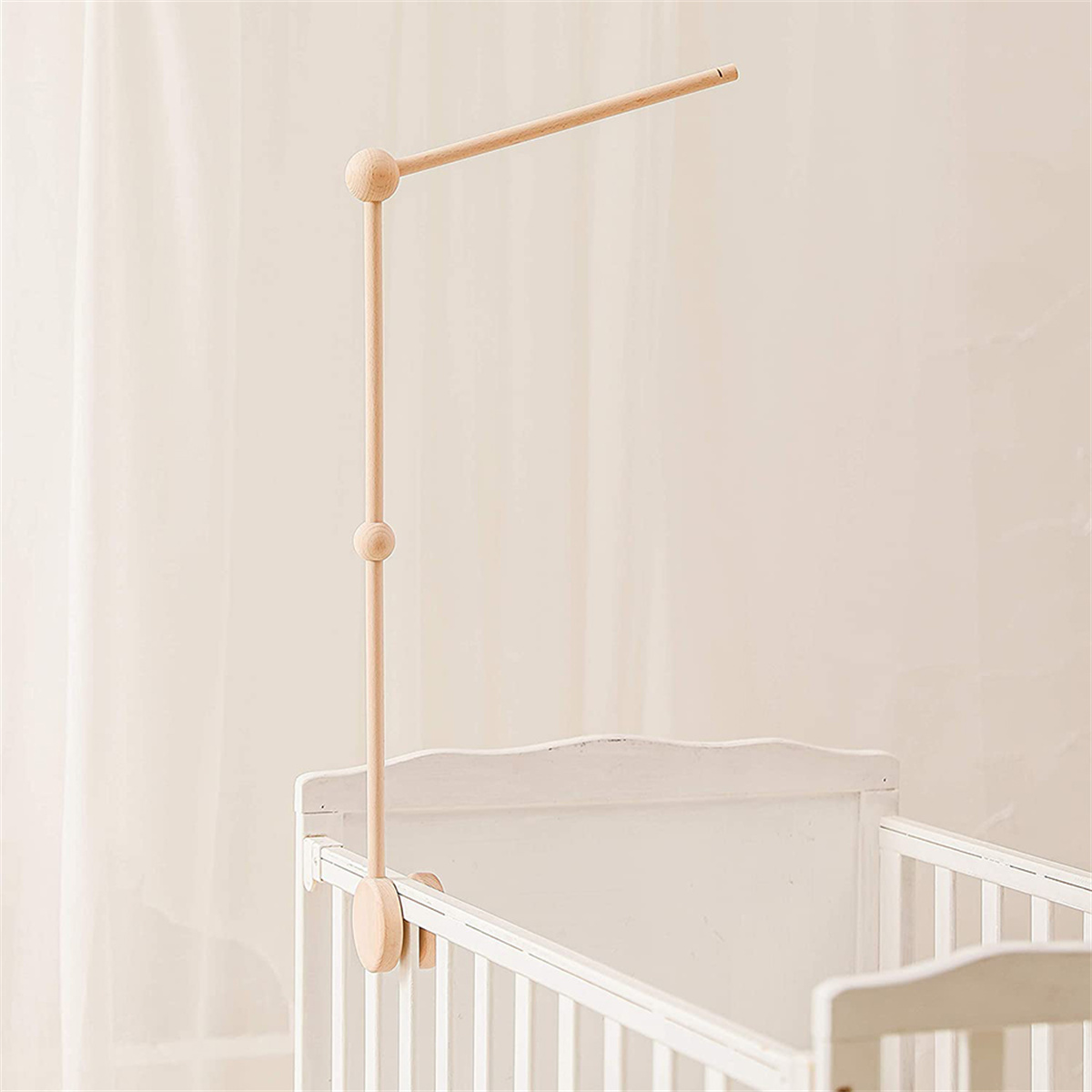 Ein hölzerner Kinderwagen-Mobilehalter, der an einem weißen Kinderbett befestigt ist.