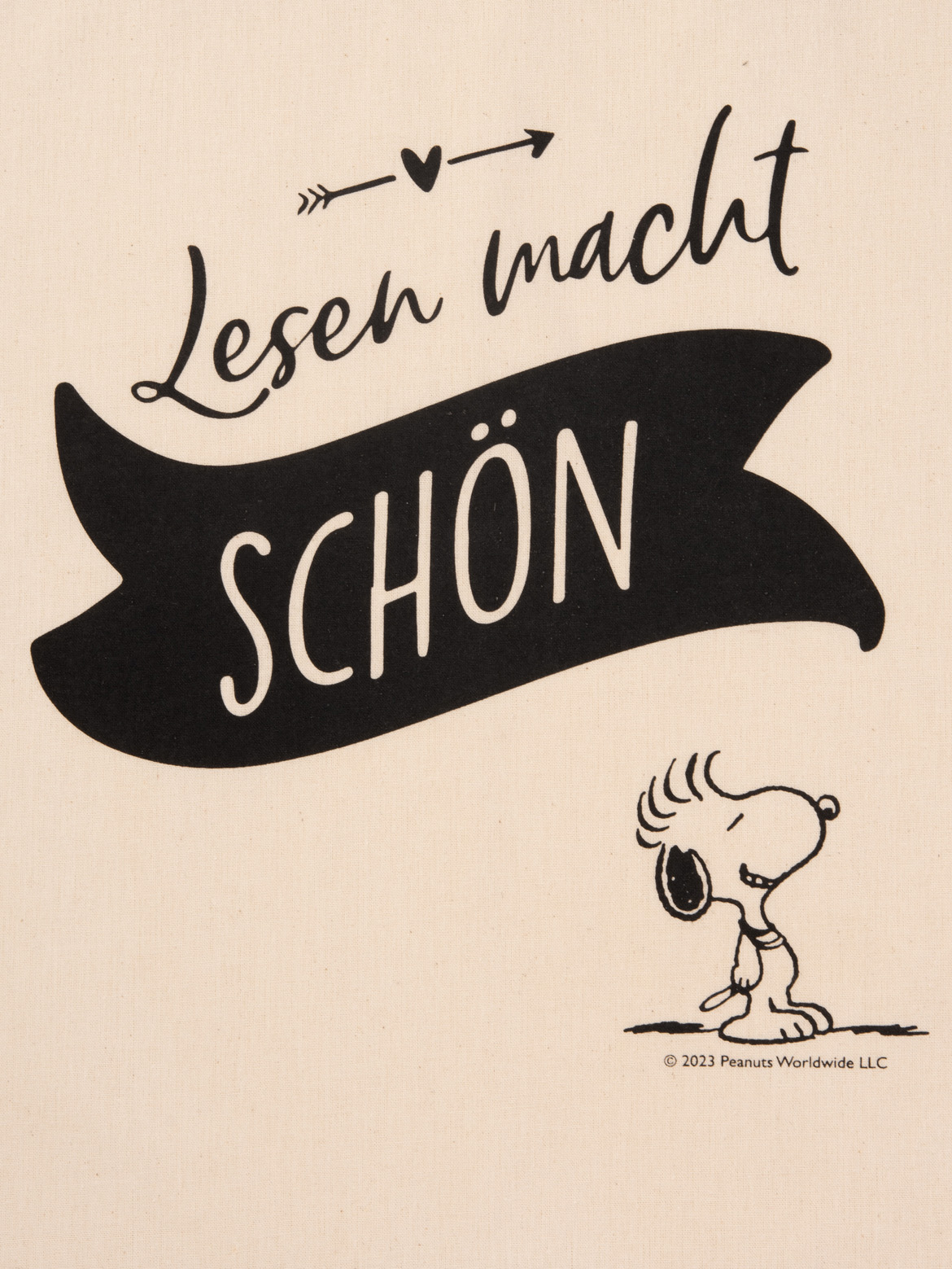Snoopy sitzt neben der Aufschrift „Lesen macht SCHÖN“ auf hellem Stoff.