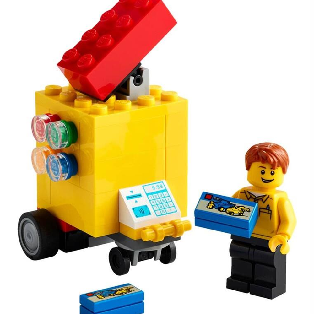 Un chiosco Lego giallo con tetto rosso e una persona Lego con scatola blu.