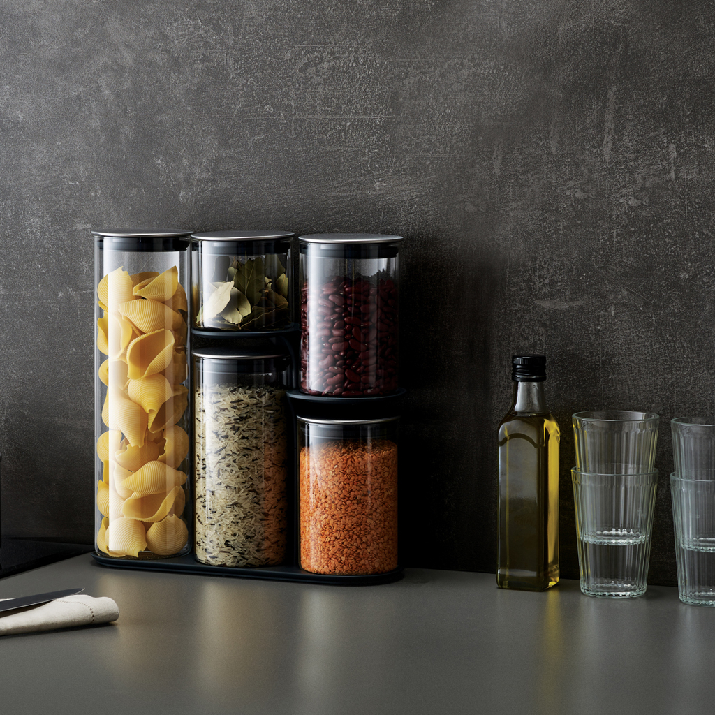 Barattoli con pasta, fagioli, riso e lenticchie accanto a olio e bicchieri.